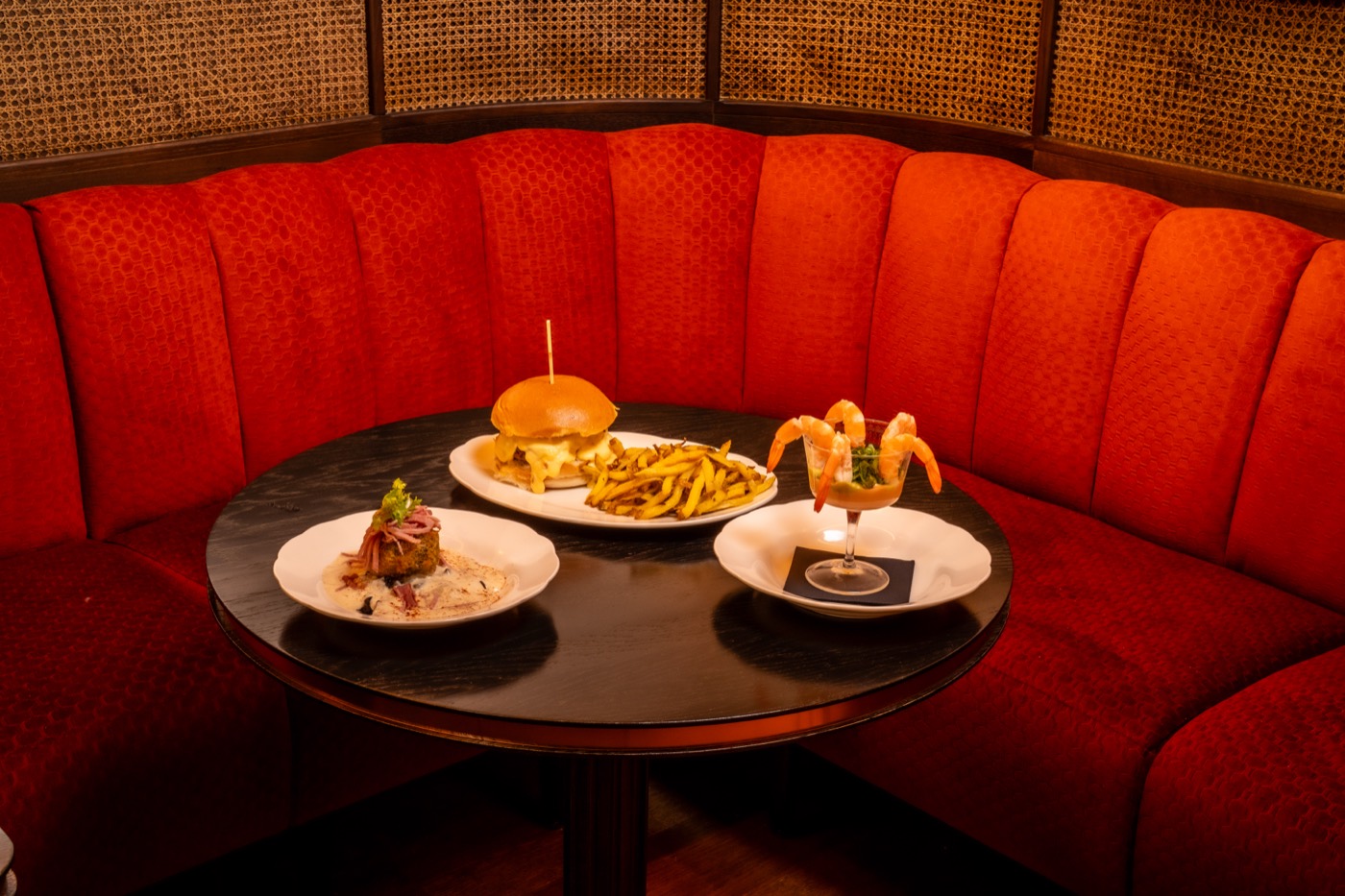 Curved red banquette, burger and prawn cocktail on a round table
