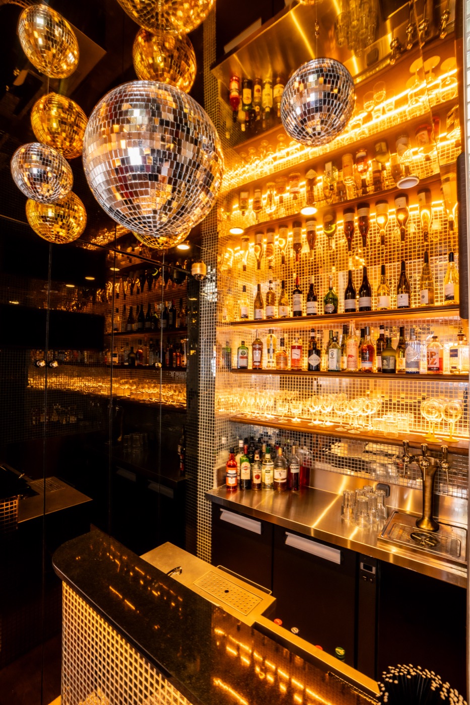 L’Émeraude, the bar at Les Causeurs, a backlit wall of bottles under the disco balls